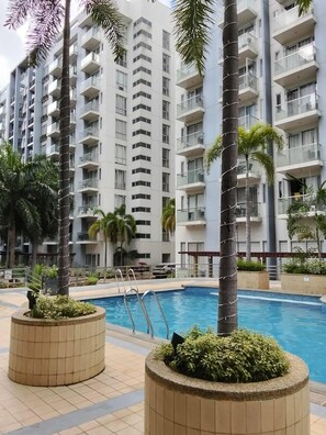 A modern residential building with multiple balconies and a swimming pool area with palm trees and planters. - XYZ’s Condo-One Palm Tree Villas, Newport: 6-Min Walk to NAIA T3 via Runway MNL (Unknown)