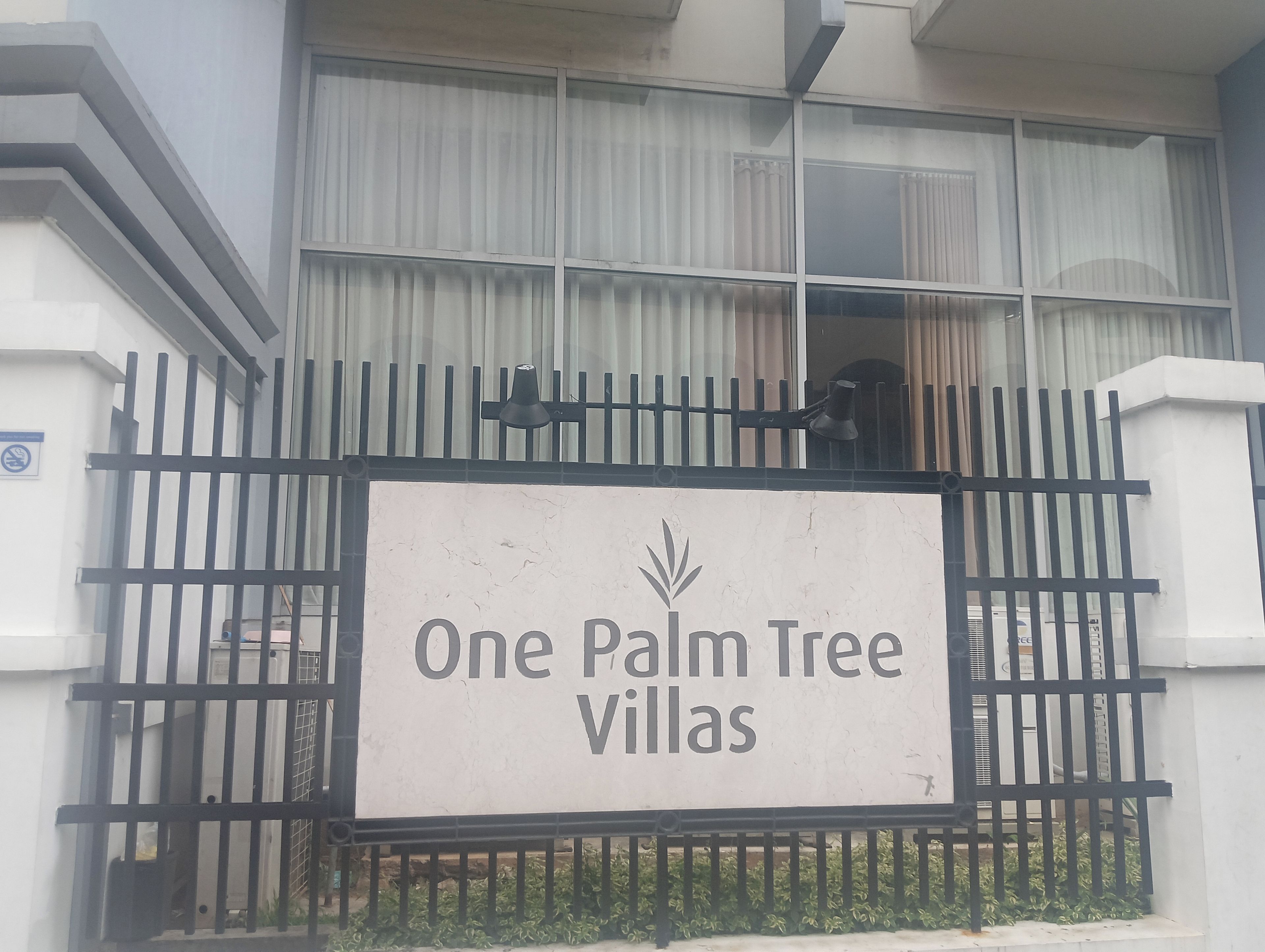 Une entrée fermée par un portail menant aux villas One Palm Tree, avec un panneau indicateur.