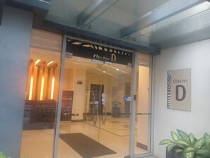 A hotel entrance with a glass door, a sign indicating 'Cluster D', and a potted plant on the right. - XYZ’s Condo-One Palm Tree Villas, Newport: 6-Min Walk to NAIA T3 via Runway MNL (Pasay)