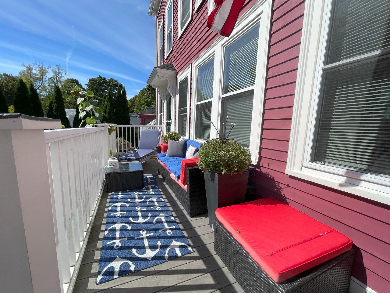 A covered outdoor seating area with a red bench, a blue and white patterned rug, and a potted plant.