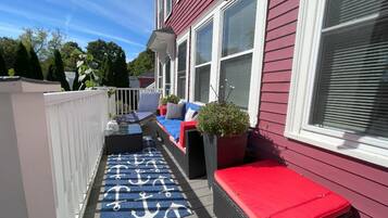 A covered outdoor seating area with a red bench, a blue and white patterned rug, and a potted plant.