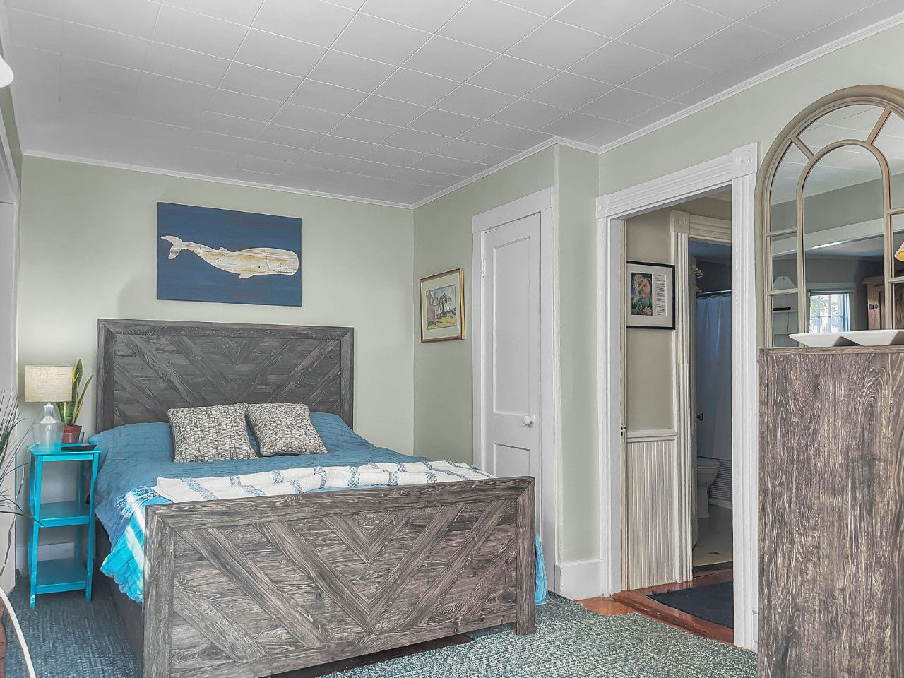 Een slaapkamer met een bed, nachtkastje, dressoir, spiegel en een muur met een schilderij.