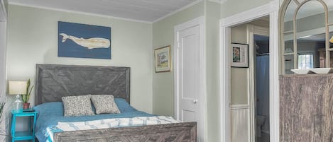 A bedroom with a bed, a nightstand, a dresser, a mirror, and a wall with a picture.