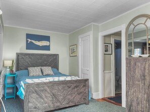 A bedroom with a bed, a nightstand, a dresser, a mirror, and a wall with a picture.