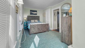 Een slaapkamer met een bed, een dressoir, een nachtkastje en een raam met jaloezieën.
