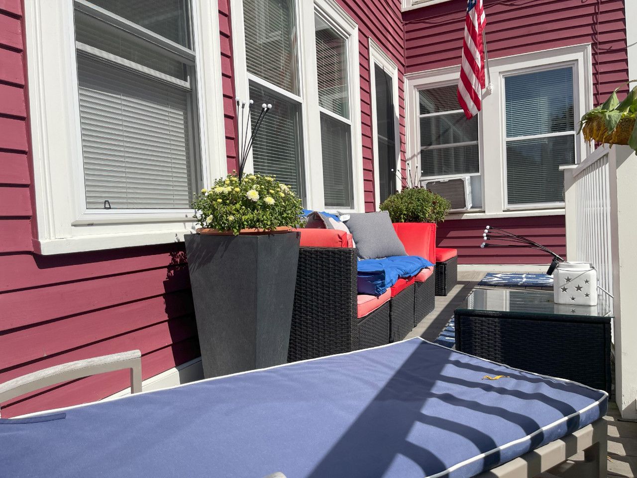 Une terrasse avec des meubles d’extérieur, une table et une chaise en osier.