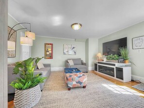 Una sala de estar con sofá, reposapiés y mueble para entretenimiento.