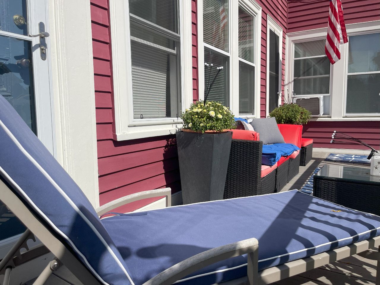A sunlit outdoor seating area with a lounge chair, a small table, and potted plants.