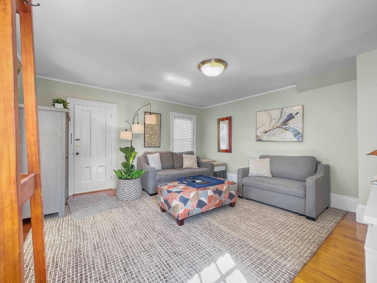 A living room with two grey sofas, a patterned ottoman, and a large rug.