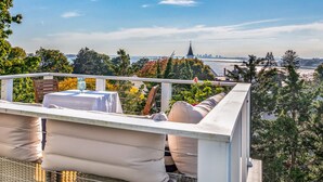 Un balcón con mobiliario exterior, una mesa y vistas a un paisaje urbano que incluye la aguja de una iglesia.