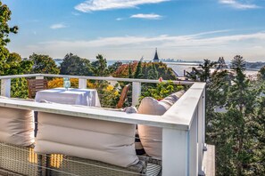 Un balcon avec un espace salon extérieur, une table et une vue sur le paysage urbain, notamment le clocher d’une église.
