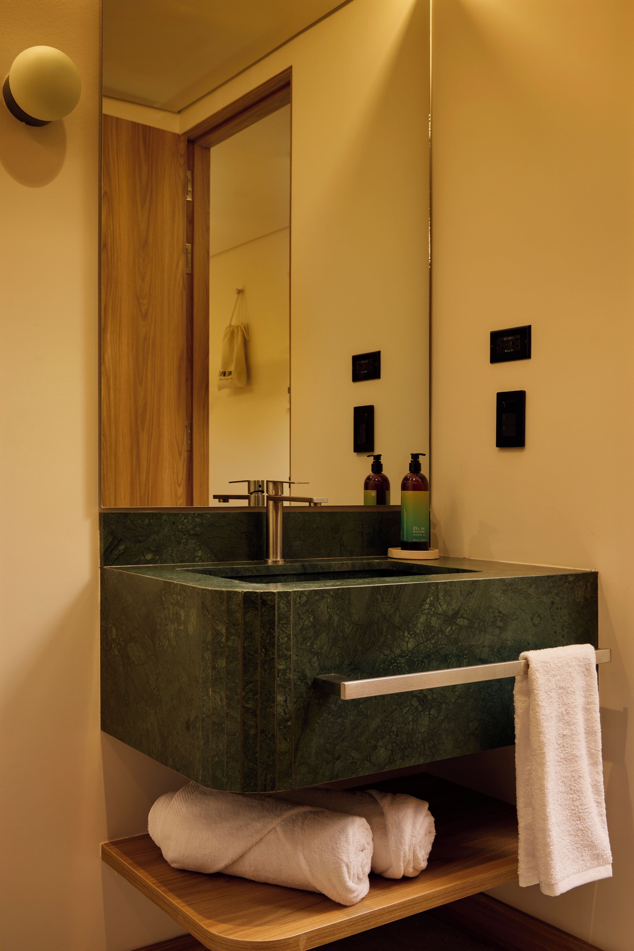 A bathroom with a dark green sink, a mirror, a towel rack, and a wooden shelf.