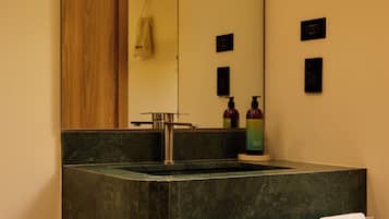 A bathroom with a dark green sink, a mirror, a towel rack, and a wooden shelf.