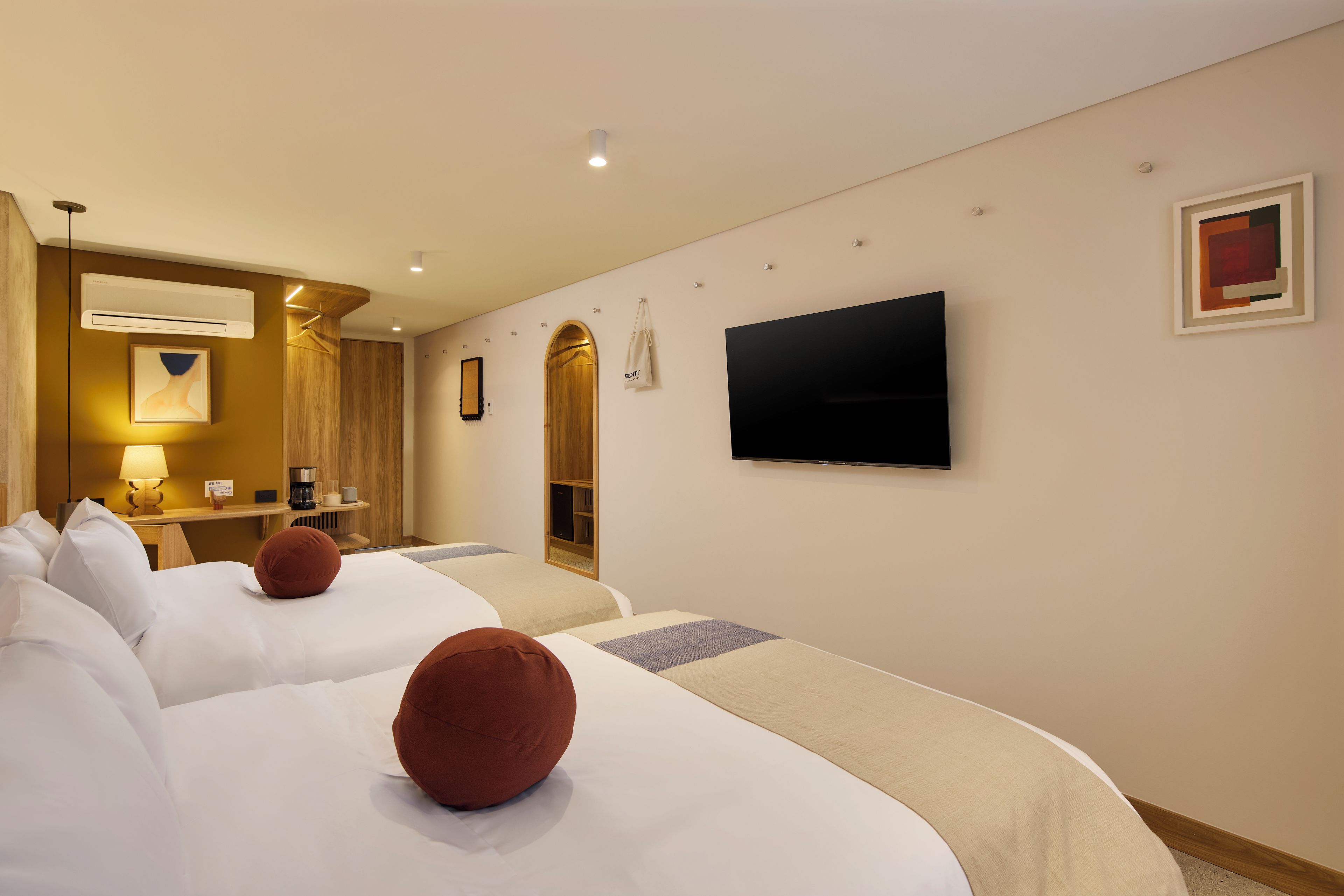 A hotel room with two beds, a TV, a mirror, and a coffee machine.
