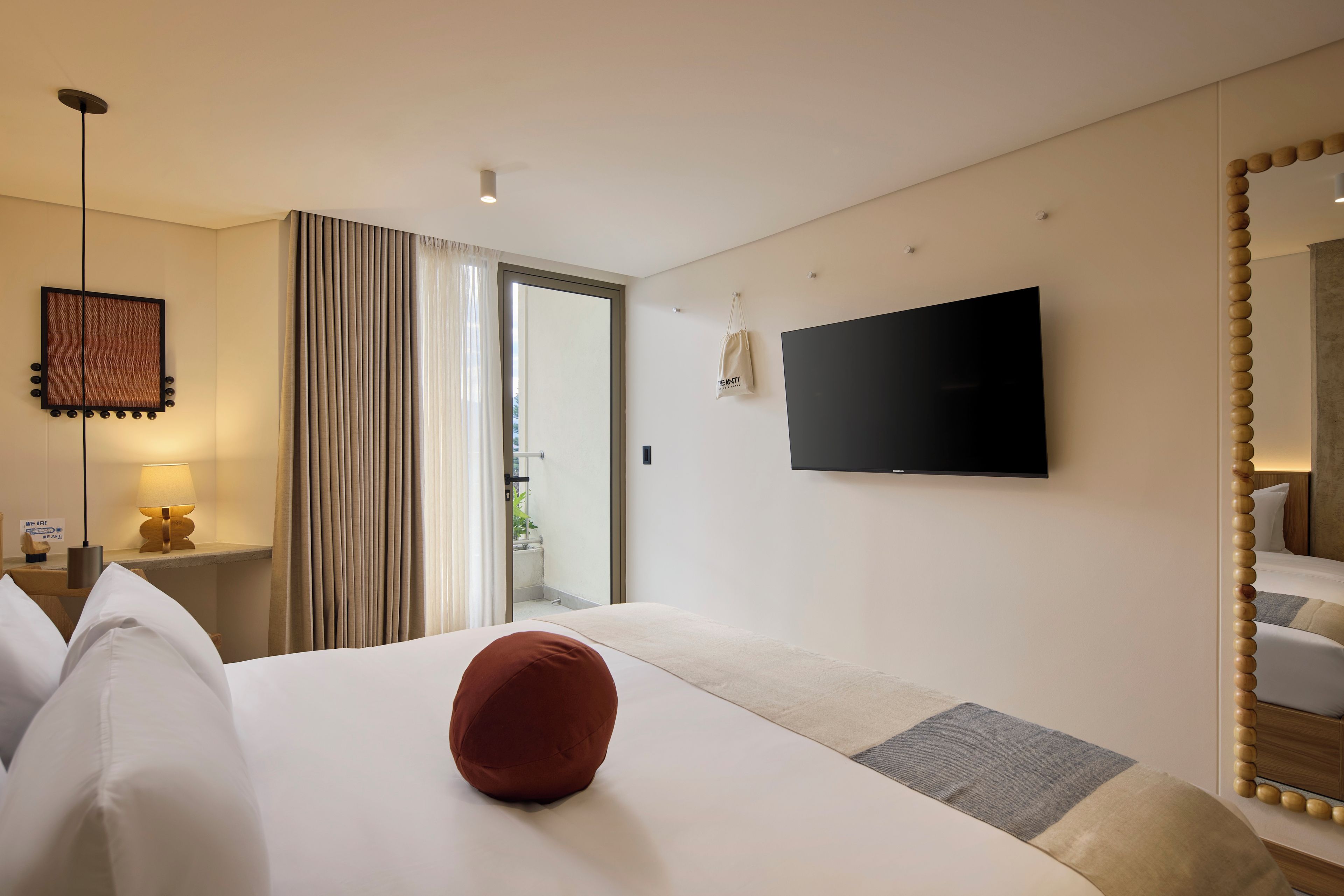 A hotel room with a bed, a television, a mirror, and a window with curtains.