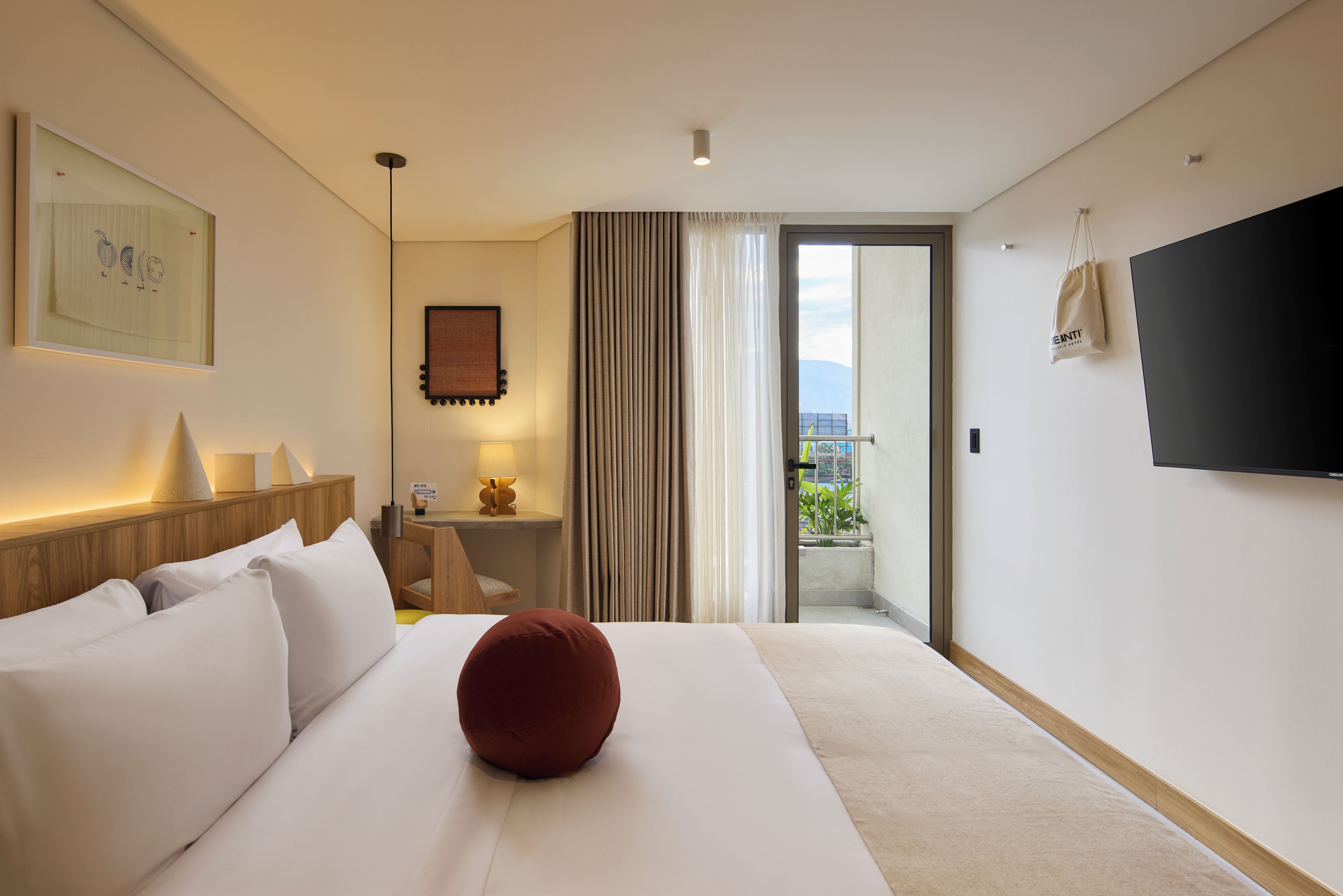 A hotel room with a bed, a TV, a window with curtains, and a view of the outdoors.