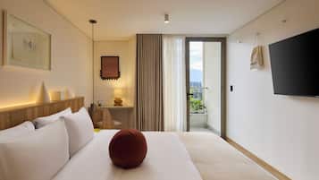 A hotel room with a bed, a TV, a window with curtains, and a view of the outdoors.
