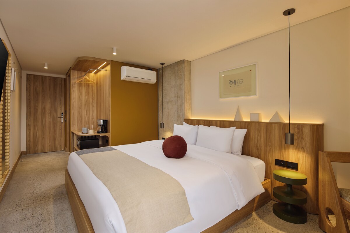 Una habitación de hotel moderna con una cama grande, una cafetera, un escritorio y un equipo de aire acondicionado.