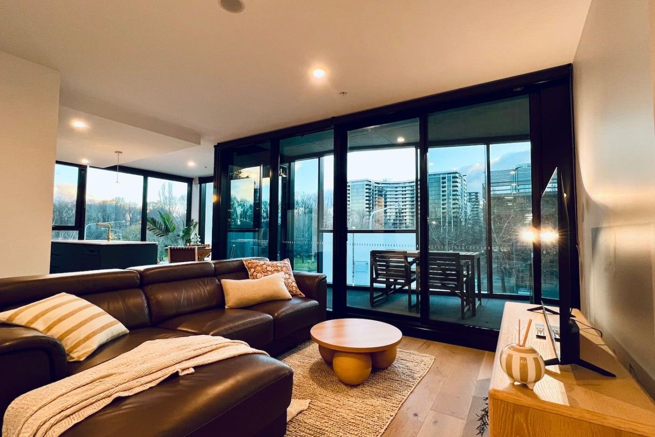 A modern living room with a leather sofa, a round coffee table, and a view of a cityscape through large windows.