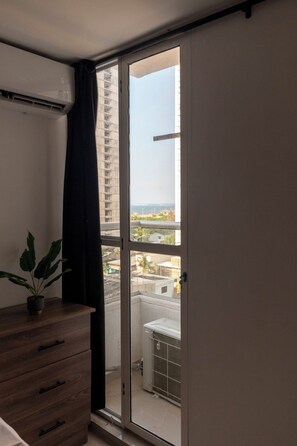 A room with a sliding glass door leading to a balcony, a wooden dresser, and a potted plant. - Cartagena Getaway | 3-Bedroom Near the Beach + Rooftop Pool (Cartagena de Indias)