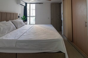 A hotel room with a large bed, a wardrobe, a window with a view of buildings, and a ceiling fan. - Cartagena Getaway | 3-Bedroom Near the Beach + Rooftop Pool (Cartagena de Indias)