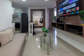 A modern living room with a sofa, a glass coffee table, a TV mounted on the wall displaying various streaming services, and a kitchen area in the background. - Cartagena Getaway | 3-Bedroom Near the Beach + Rooftop Pool (Cartagena de Indias)