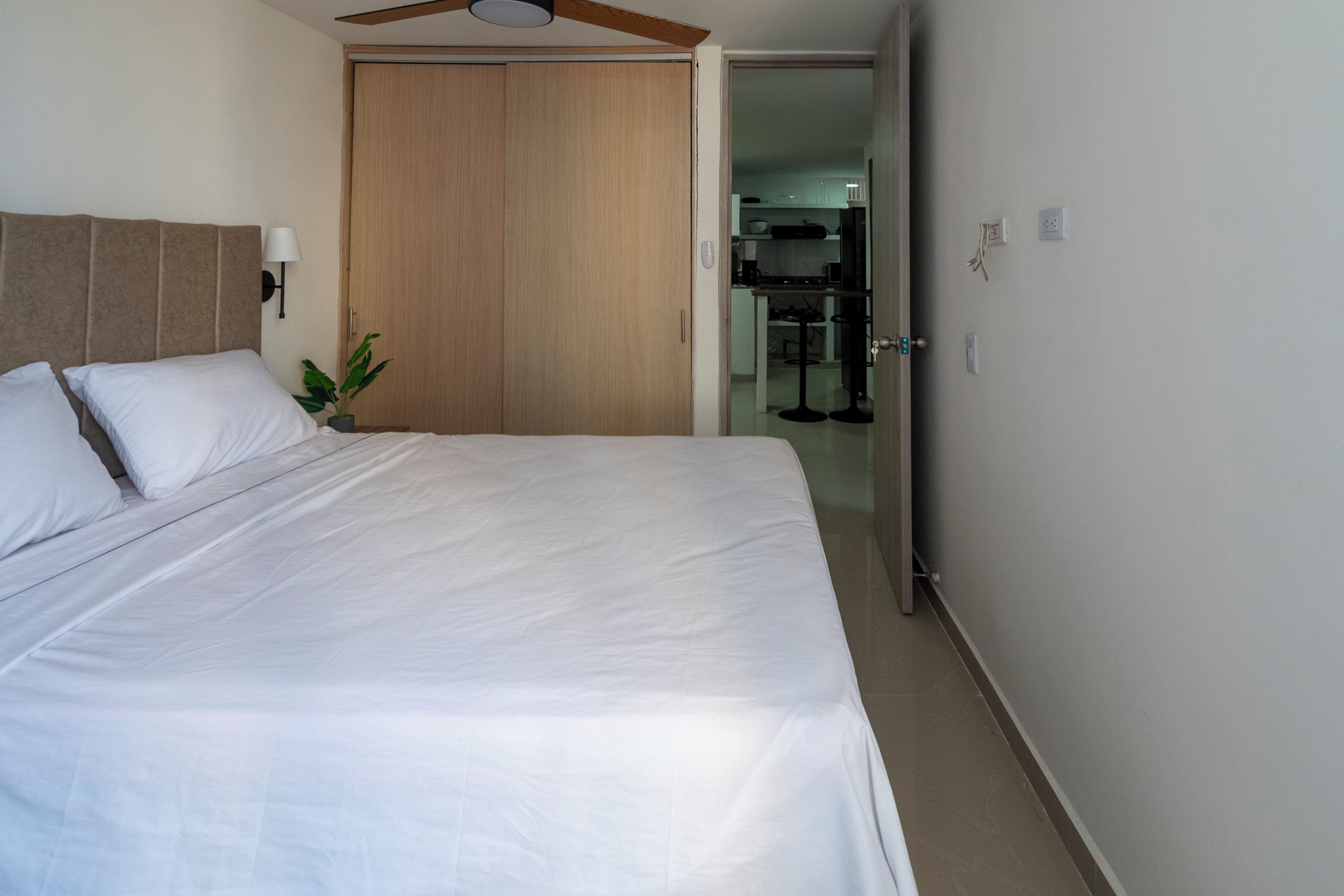 Een hotelkamer met een bed, een plafondventilator, een houten garderobe en een kleine plant.