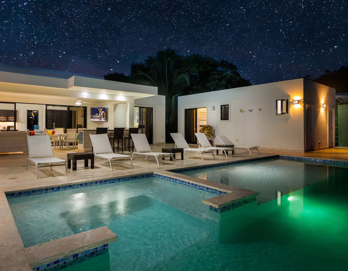A swimming pool with lounge chairs and a bar area, under a night sky with stars.