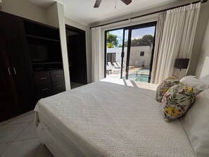 Ein Schlafzimmer mit Bett, Fernseher, Kleiderschrank und Blick auf einen Pool sowie Sitzgelegenheiten im Freien.