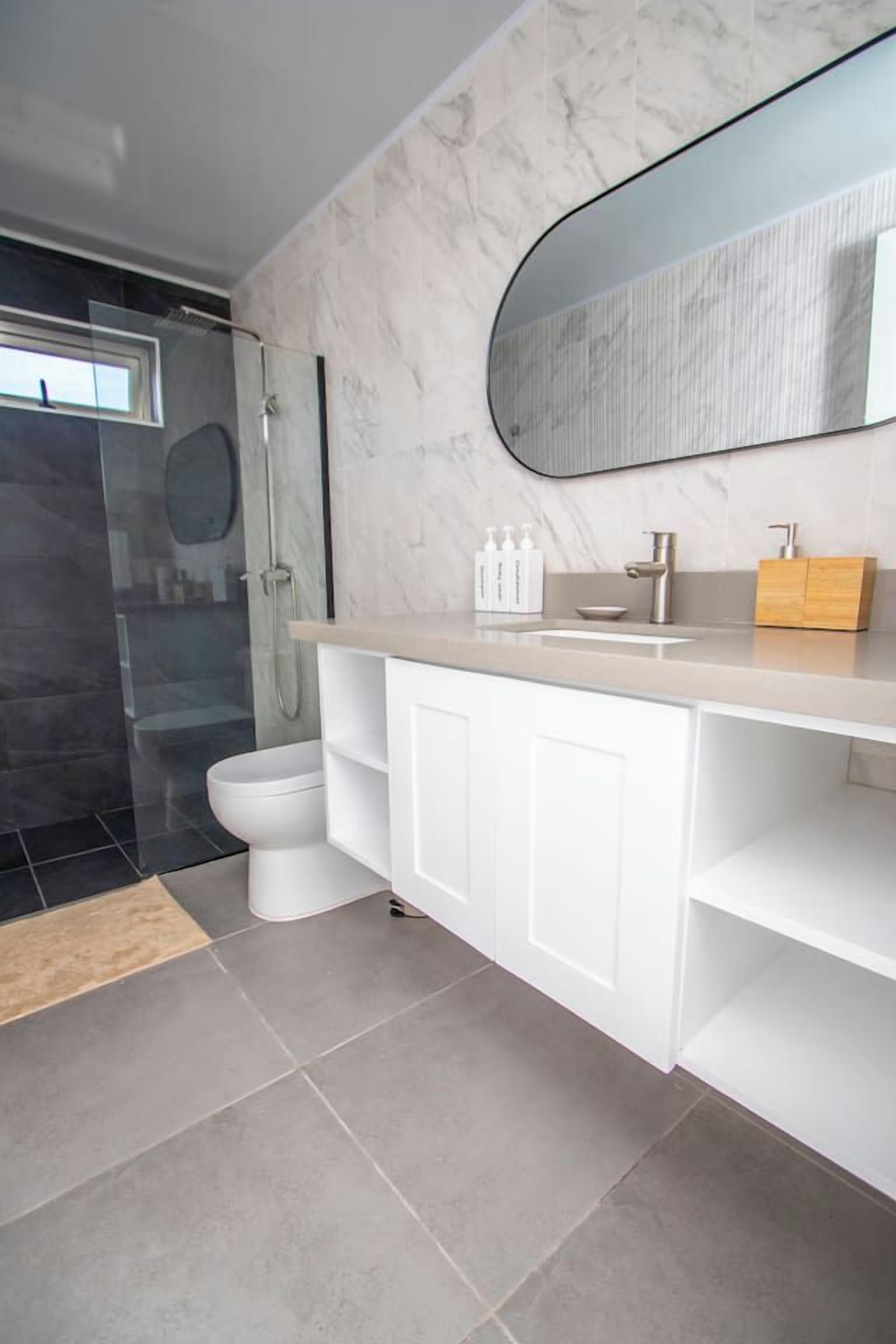 A modern bathroom with a glass shower enclosure, a toilet, a vanity with a mirror, and a sink.