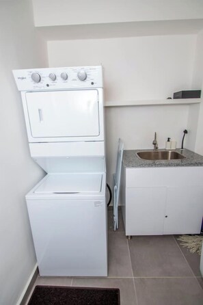 A compact laundry area with a stacked washer and dryer, a small sink, and a cabinet. - Stylish New 2-Bedroom Apartment with Pools & Gym (Cabarete)