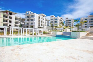 A modern hotel with a swimming pool, multiple balconies, and a landscaped garden area. - Stylish New 2-Bedroom Apartment with Pools & Gym (Cabarete)