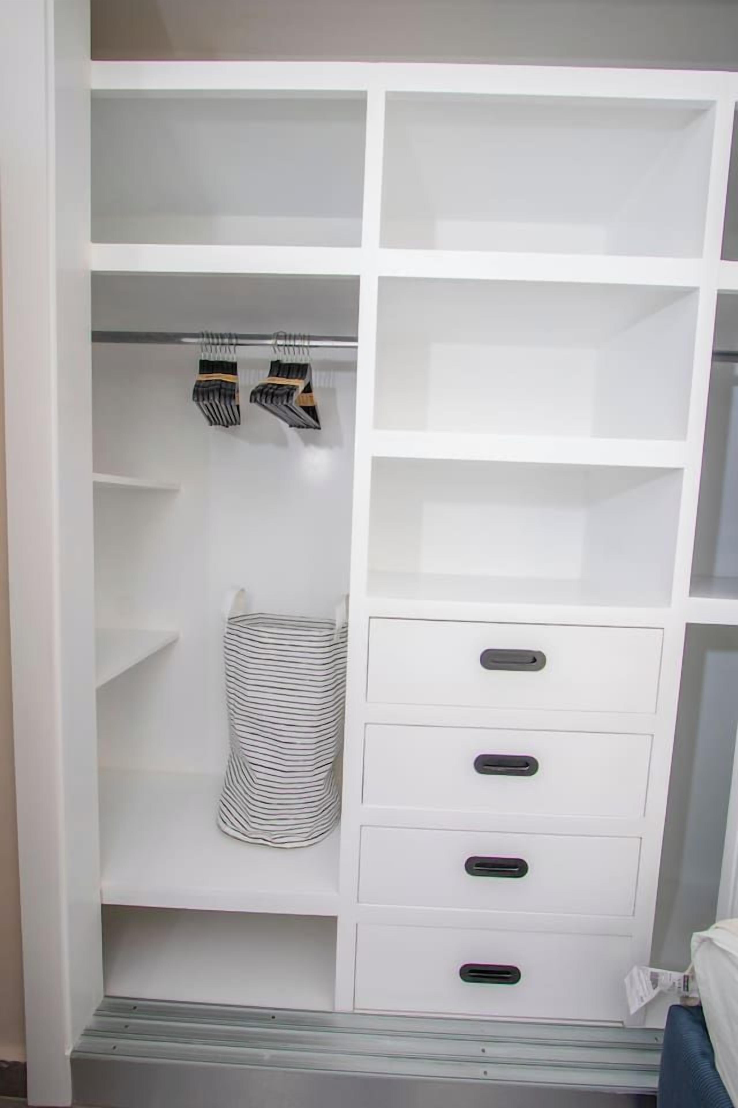 A white closet with multiple shelves and drawers, a striped hanging bag, and a pair of striped socks.