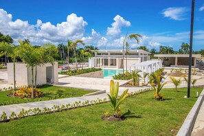 A modern building with a pool, surrounded by palm trees and greenery. - Stylish New 2-Bedroom Apartment with Pools & Gym (Cabarete)