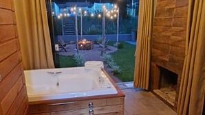 Un baño con una bañera de madera, una alfombra roja y vistas a un jardín por la noche.
