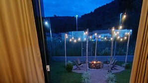 Habitación con una bañera grande, piso de madera y vista a un jardín paisajístico al atardecer.