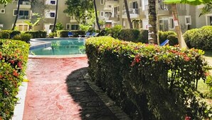 A pool area with a red pathway, surrounded by palm trees and a multi-story building with balconies. - Gran sol caribe corales punta cana (Punta Cana)