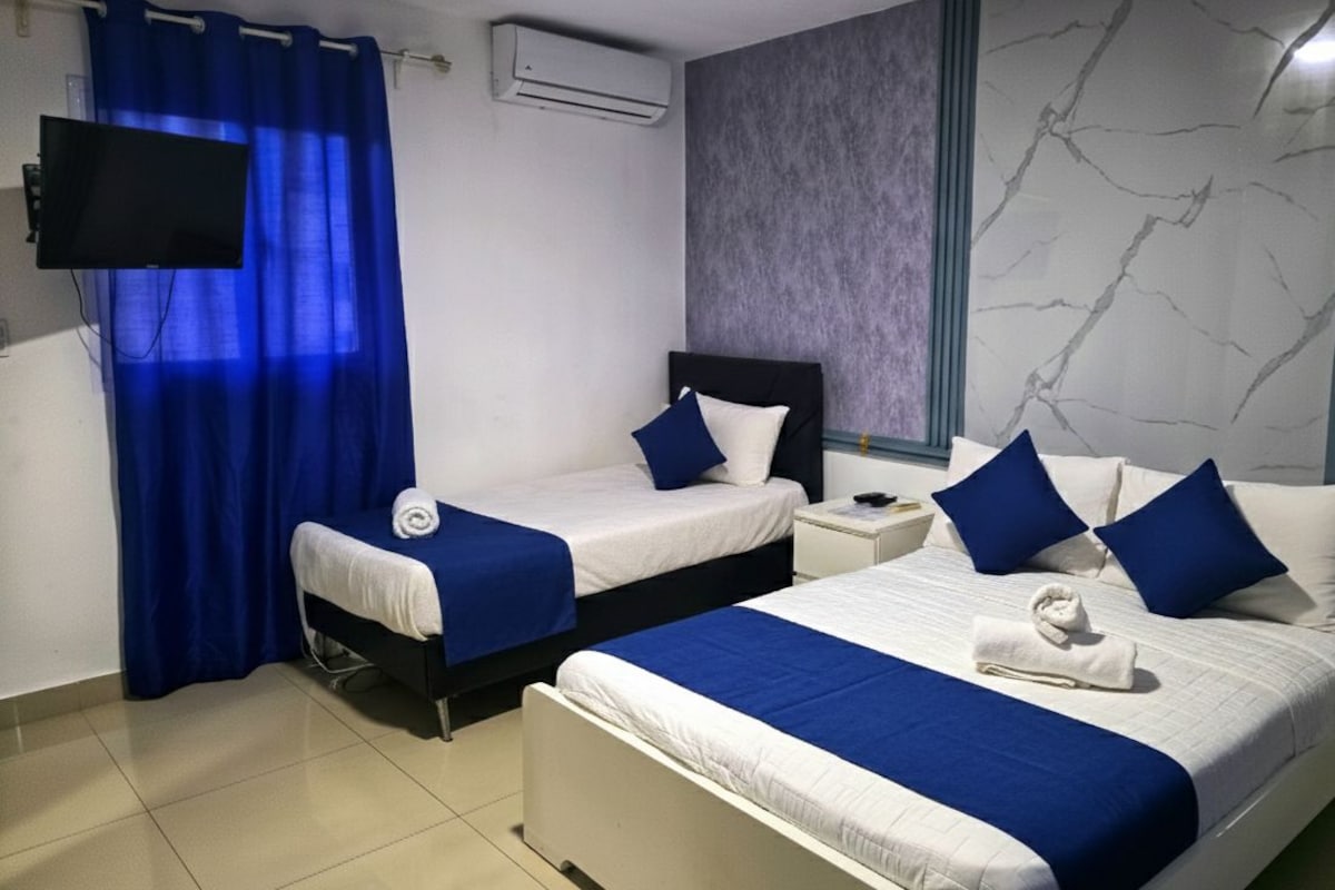 Habitación de hotel con dos camas, un televisor de pantalla plana, una ventana con cortinas y una pared con diseño de mármol.