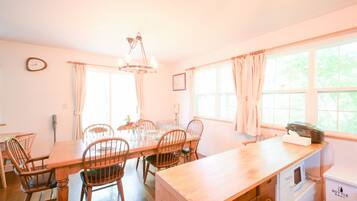 A dining area with a wooden table and chairs, a chandelier, and a kitchen area with a microwave and a refrigerator.