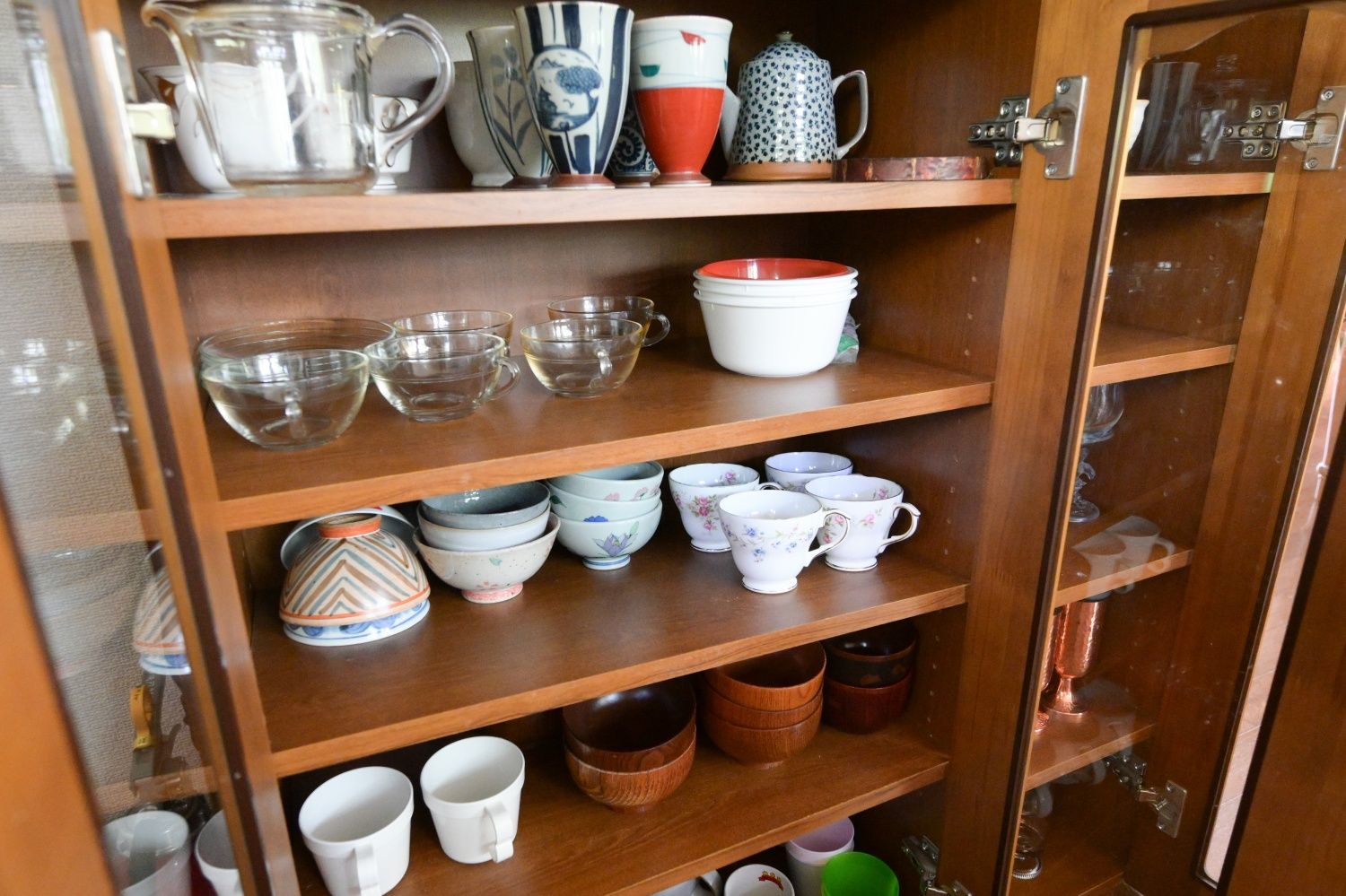 A wooden cabinet with shelves holding various ceramic cups and bowls.