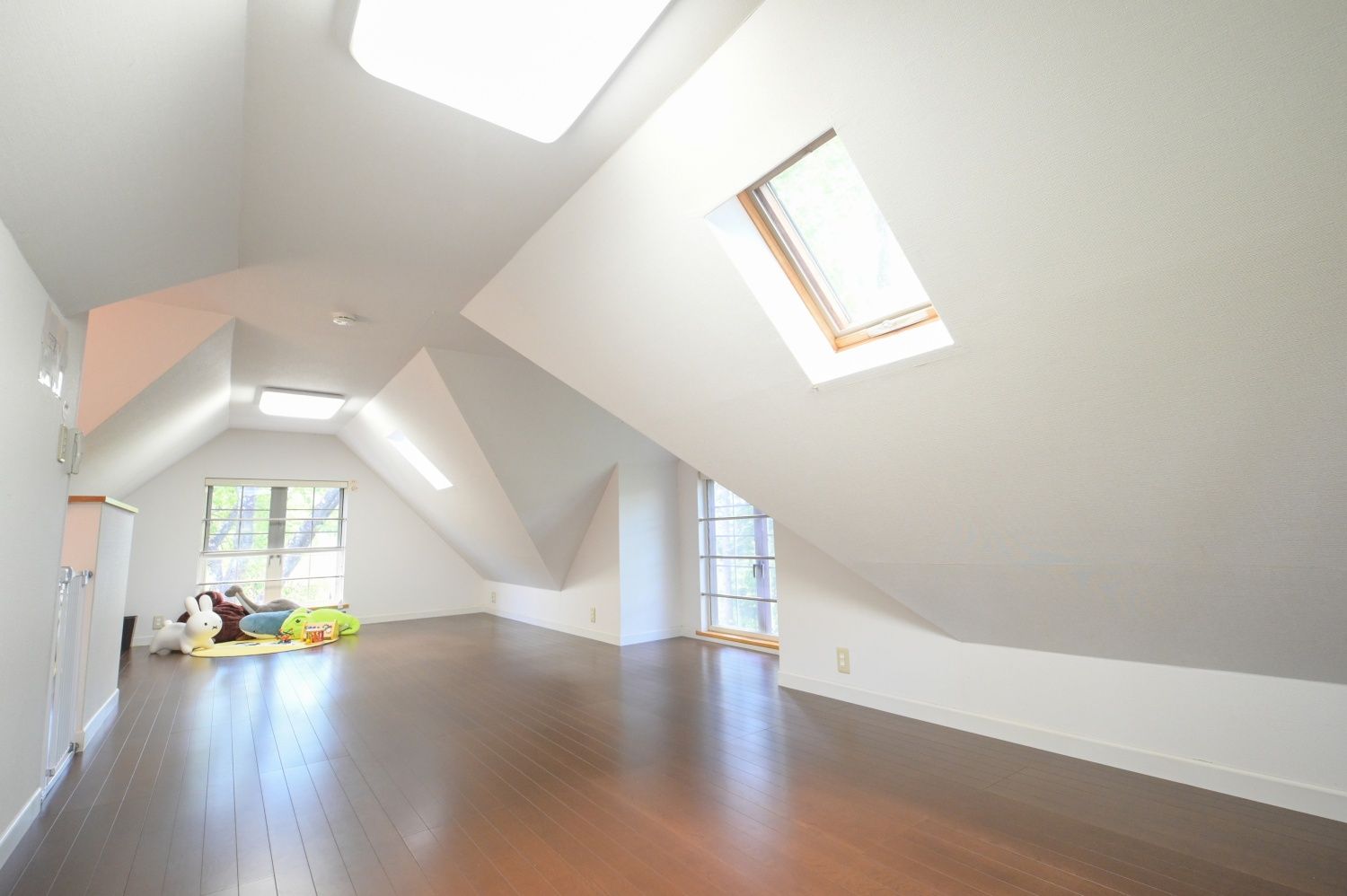 A spacious attic room with high ceilings, skylights, and hardwood floors.