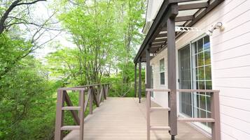 A wooden deck leading to a building with large windows, surrounded by lush greenery.