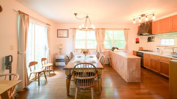 A spacious kitchen with wooden cabinets, a dining table set for six, and a large window providing natural light. - Yatsugatake Angel AG1 (Hokuto)