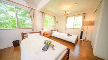 A hotel room with two beds, a wooden floor, a window with curtains, a bedside lamp, and a small trash bin.