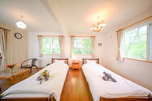 A hotel room with two single beds, a wooden floor, a table with a vase of flowers, and a chair. - Yatsugatake Angel AG1 (Hokuto)