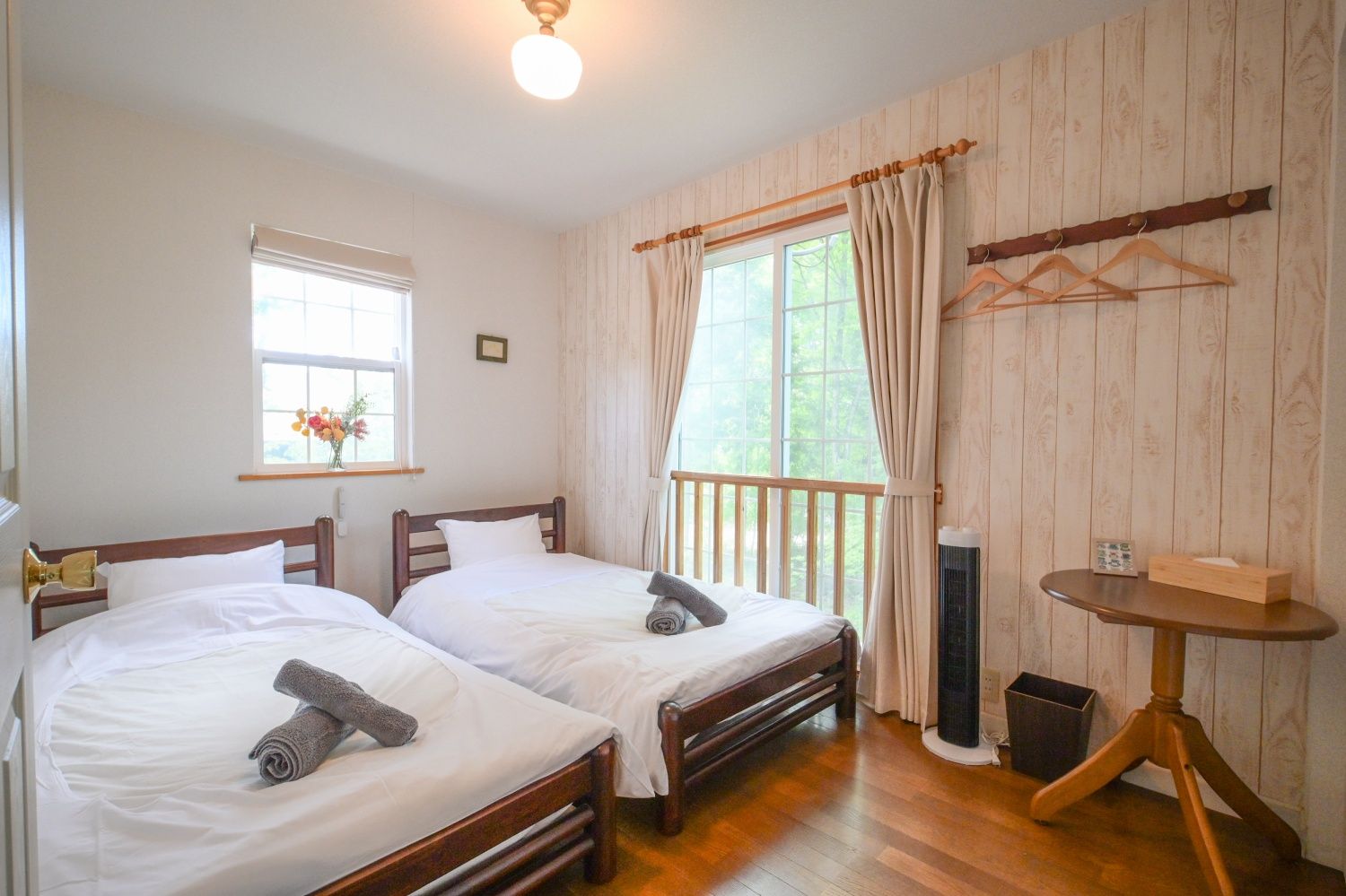 A room with two beds, a small table, and a window with curtains.