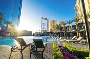 Un espace piscine d’hôtel avec des chaises longues et un grand panneau publicitaire pour l’hôtel Elara.