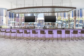 Eine Bar mit einer gebogenen Theke, mehreren Barhocker und Blick auf die Stadt durch große Fenster.
