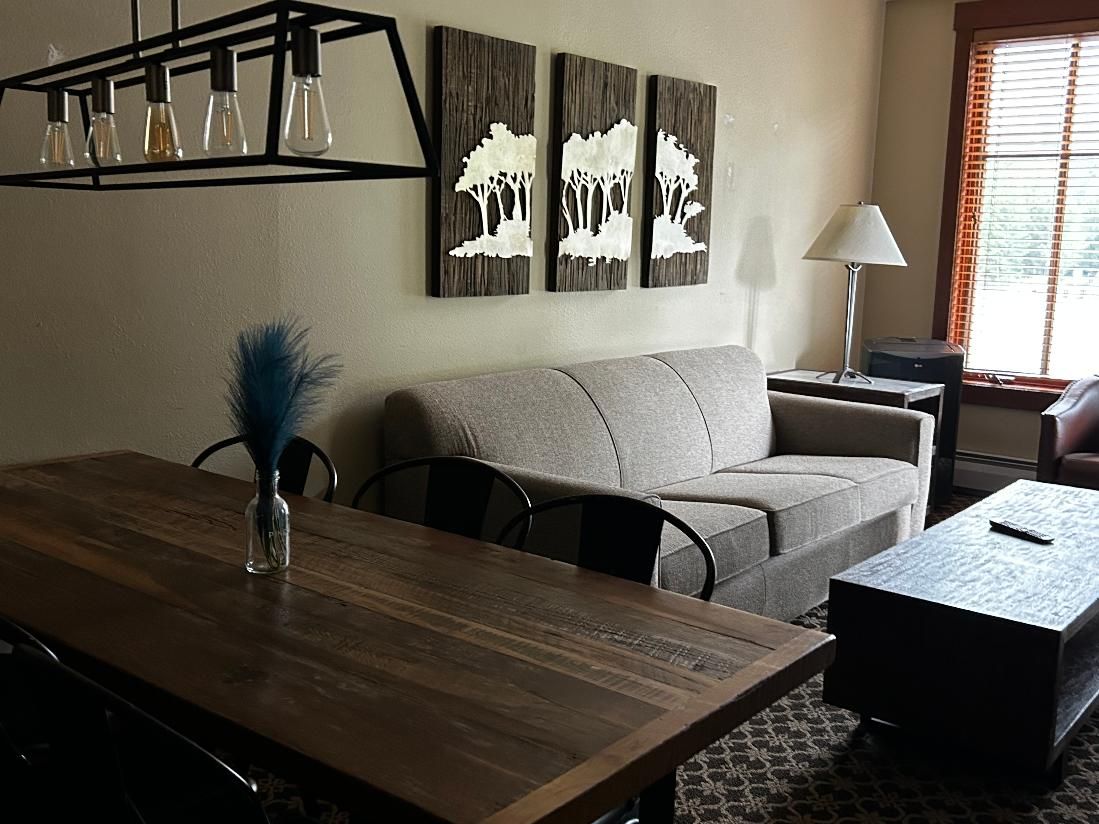 A living room with a wooden dining table, a sofa, a coffee table, and wall art.