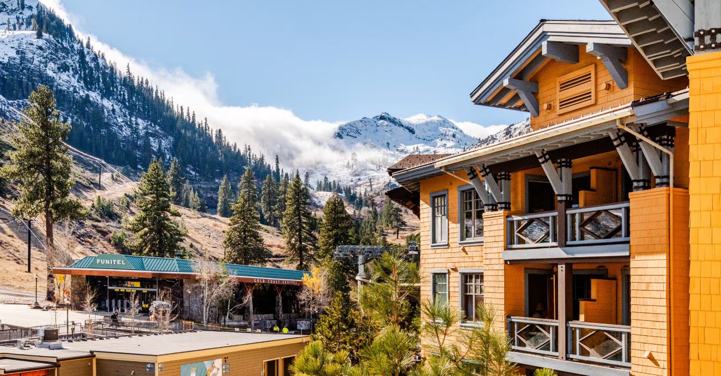 A mountain lodge with a wooden facade, a covered outdoor seating area, and a view of snow-capped mountains.